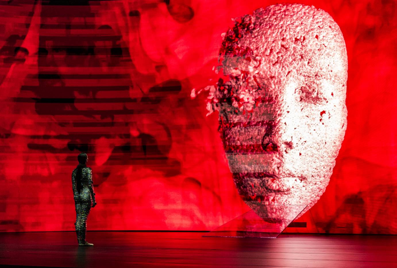 Female dancer stares at mask projected on red background